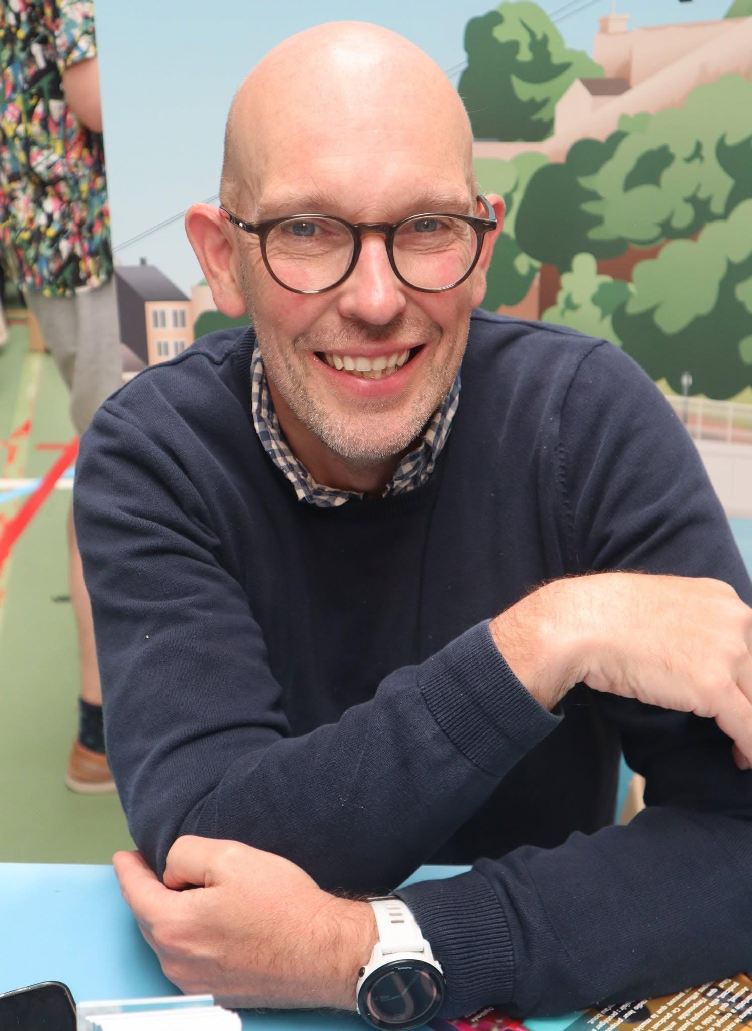 Olivier Moreaux, smiling, round glasses and navy sweater, seated at a book-signing table